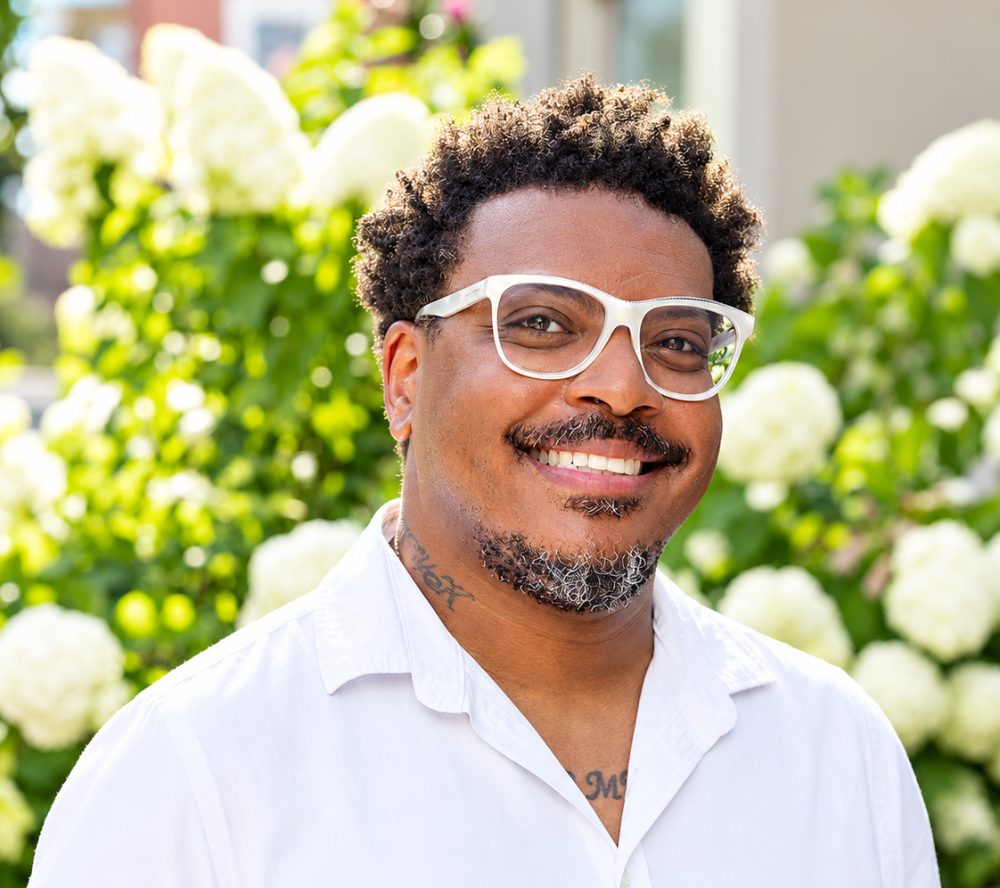 Thomas Kelly, owner of Creative Soulz Printing, smiling outdoors in a white shirt